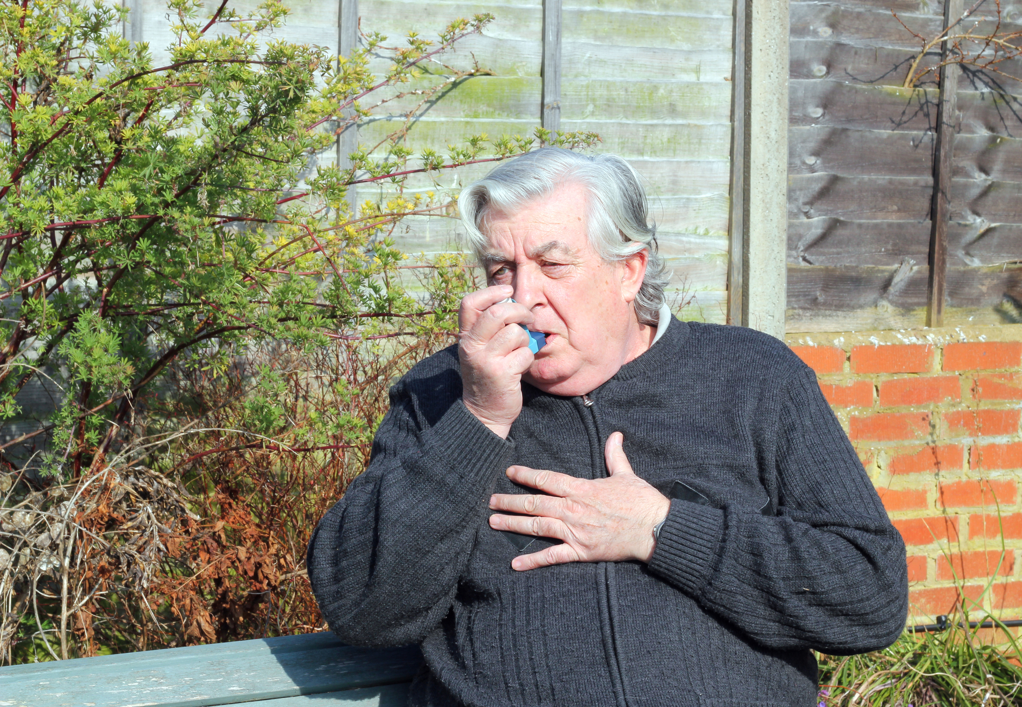 older man on a bench breathing with an inhaler