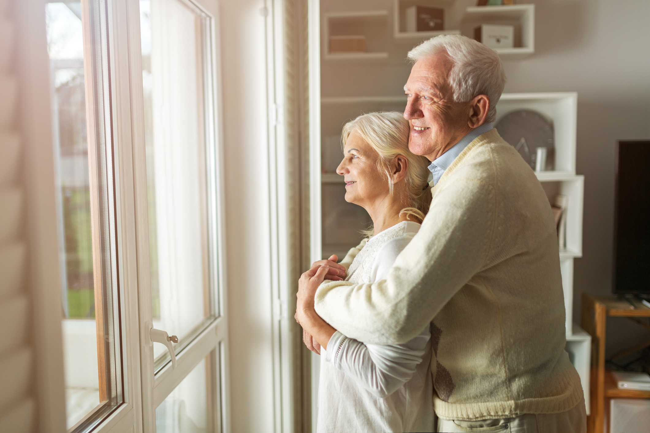 elderly couple embracing and looking out a window