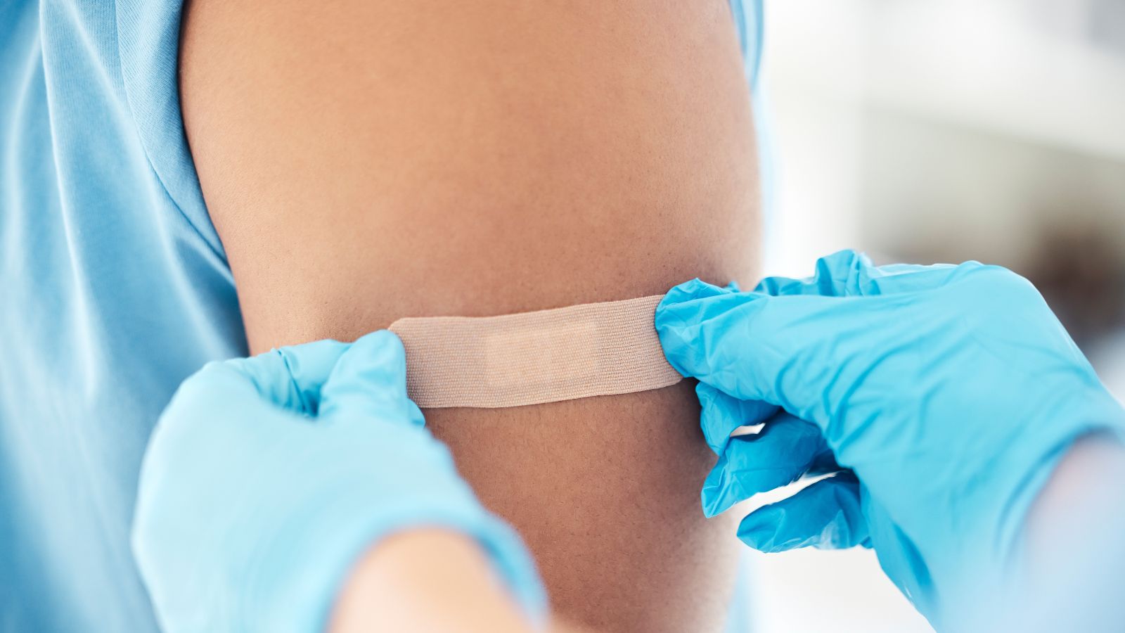 Gloved hands placing a band-aid on a patient's arm after they received a flu shot